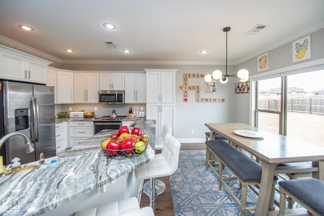 kitchen with crown molding, appliances with stainless steel finishes, white cabinetry, and a breakfast bar