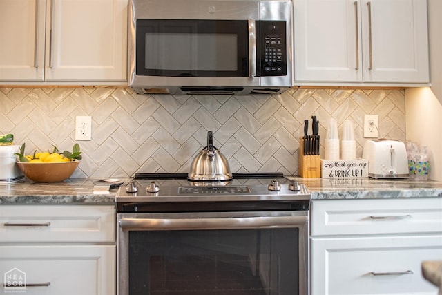 kitchen featuring tasteful backsplash, white cabinets, appliances with stainless steel finishes, and light stone countertops