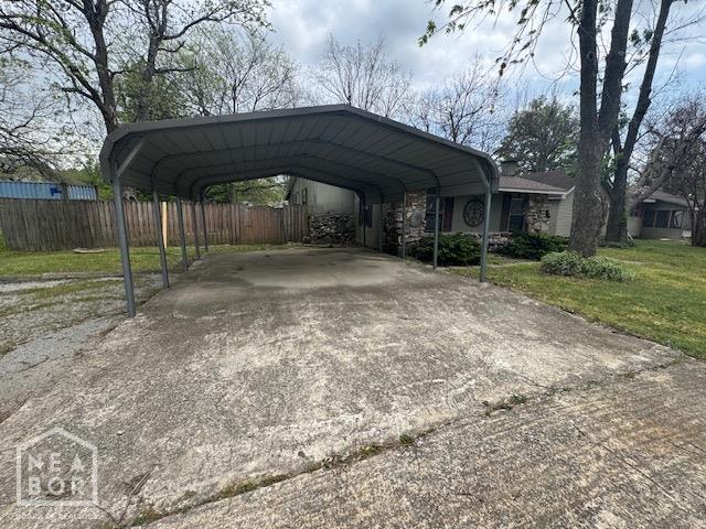 view of parking / parking lot featuring concrete driveway, fence, and a carport