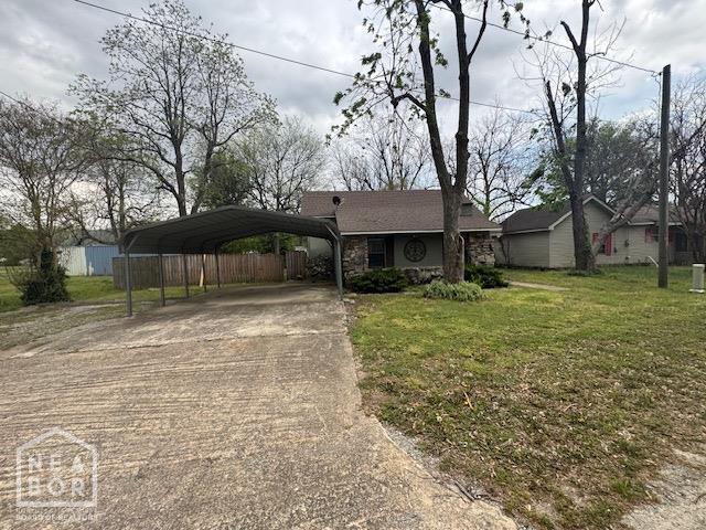 ranch-style house with concrete driveway, a front lawn, a carport, stone siding, and fence