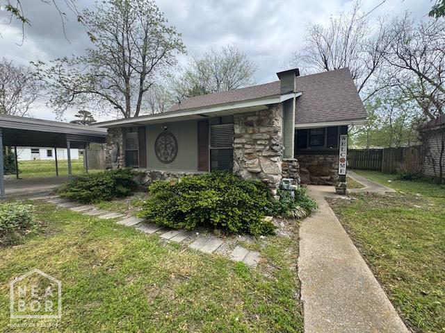 bungalow-style home with stone siding, a front yard, fence, and a shingled roof