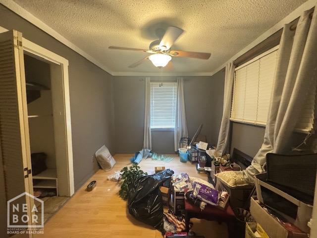 bedroom with wood finished floors, a textured ceiling, a ceiling fan, and ornamental molding
