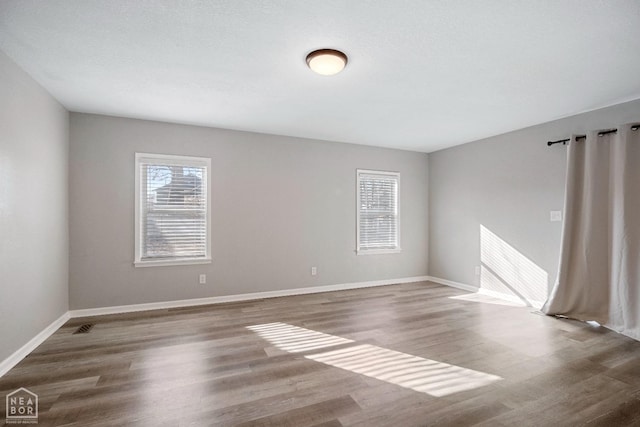 empty room with plenty of natural light, wood finished floors, and baseboards