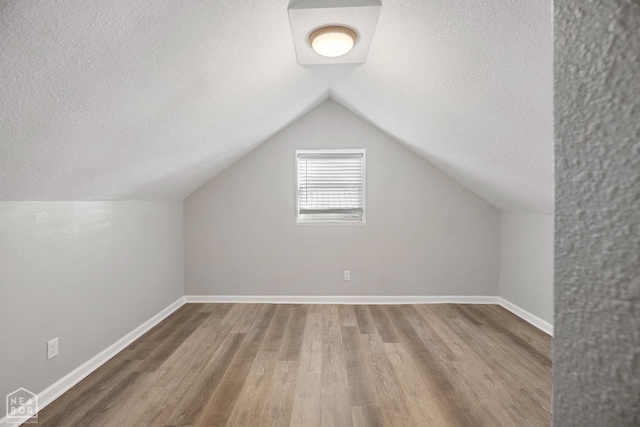 additional living space featuring wood finished floors, a textured ceiling, lofted ceiling, and baseboards
