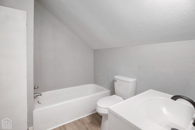 bathroom featuring lofted ceiling, wood finished floors, toilet, a tub, and a sink