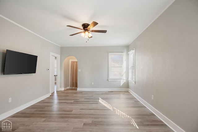 unfurnished living room featuring a ceiling fan, arched walkways, wood finished floors, ornamental molding, and baseboards
