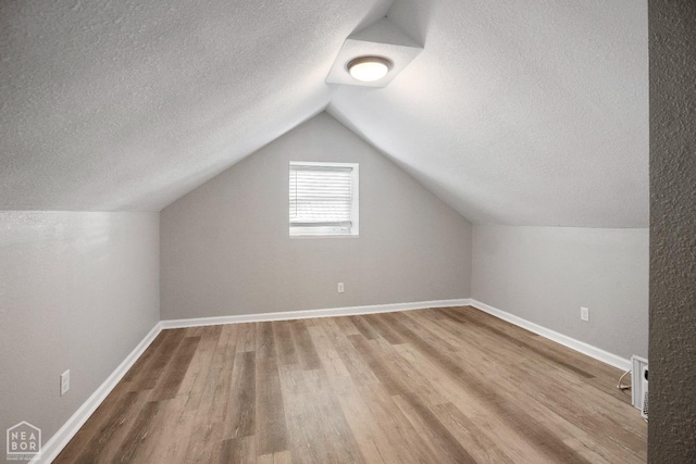 additional living space with a textured ceiling, wood finished floors, lofted ceiling, and baseboards