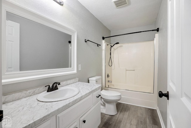 bathroom with wood finished floors, vanity, toilet,  shower combination, and a textured ceiling