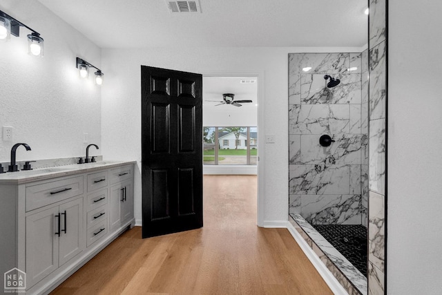 full bathroom featuring visible vents, a ceiling fan, wood finished floors, a sink, and a marble finish shower