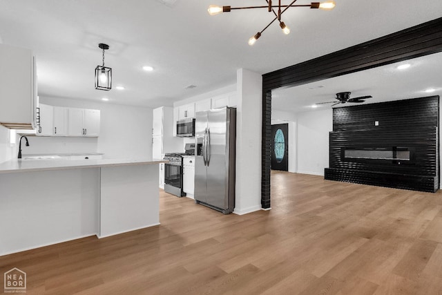 kitchen featuring appliances with stainless steel finishes, a sink, light wood finished floors, a large fireplace, and open floor plan