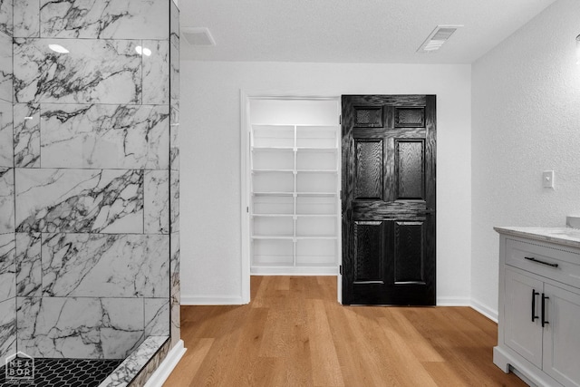 full bathroom featuring visible vents, a tile shower, wood finished floors, vanity, and baseboards