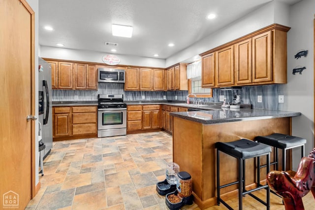 330 Greene 730th Rd, Paragould, AR 72450 - kitchen with appliances with stainless steel finishes, a peninsula, brown cabinets, decorative backsplash, and a breakfast bar area