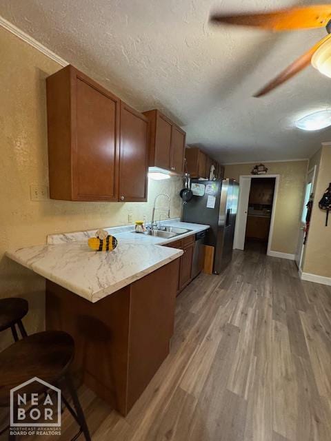 1207 Basil St, Corning, AR 72422 - kitchen with stainless steel refrigerator with ice dispenser, light wood-type flooring, a textured ceiling, a breakfast bar, and brown cabinetry