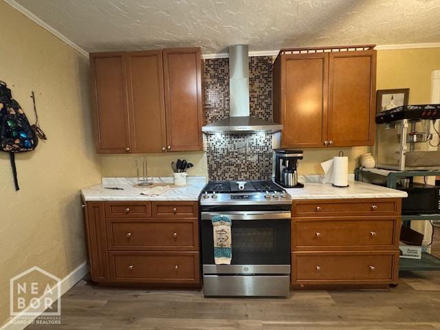 1207 Basil St, Corning, AR 72422 - kitchen with gas stove, wall chimney range hood, ornamental molding, brown cabinets, and light wood finished floors