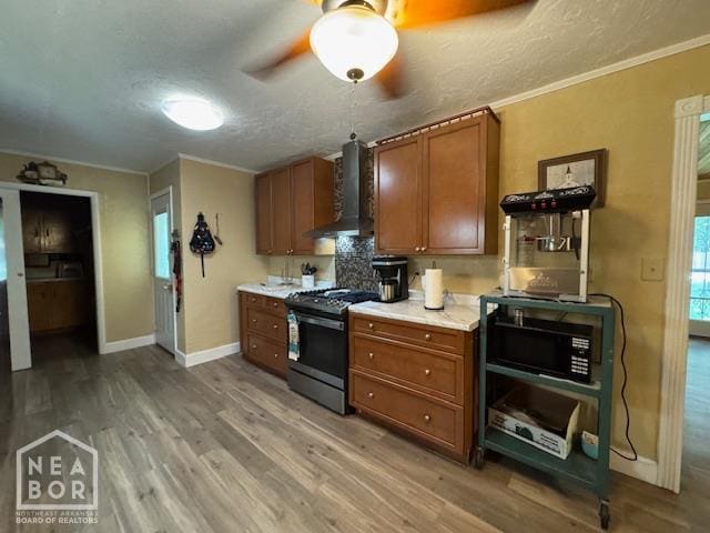 1207 Basil St, Corning, AR 72422 - kitchen featuring stainless steel gas range oven, wall chimney range hood, brown cabinetry, light wood-style floors, and light countertops
