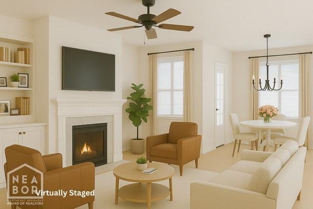 living area featuring ceiling fan with notable chandelier, built in shelves, a lit fireplace, and a healthy amount of sunlight