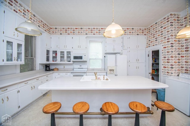 kitchen with washer / clothes dryer, a kitchen breakfast bar, wallpapered walls, white appliances, and a sink
