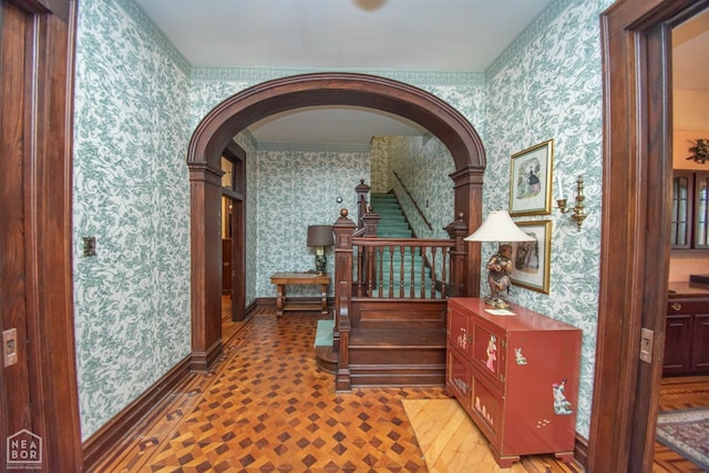 hallway featuring arched walkways, wallpapered walls, baseboards, and stairs