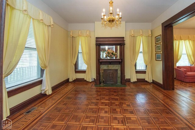unfurnished living room with baseboards, an inviting chandelier, a fireplace with flush hearth, and a healthy amount of sunlight