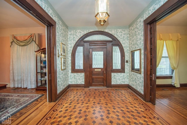 entryway featuring baseboards, a notable chandelier, and wallpapered walls