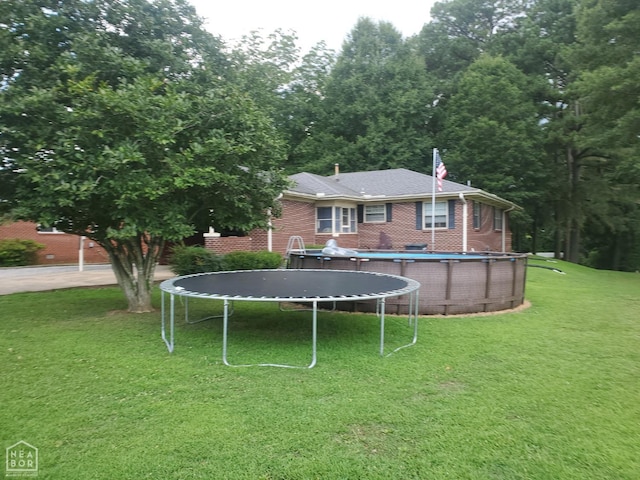 691 Crestline Dr, Piggott, AR 72454 - rear view of house featuring a trampoline, a yard, brick siding, and an outdoor pool