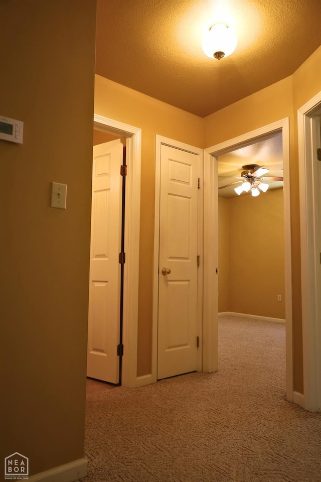 hallway featuring carpet floors, baseboards, and a textured ceiling