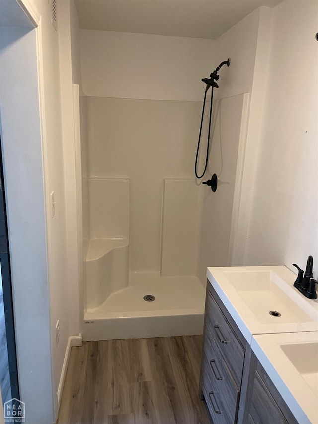 bathroom featuring visible vents, double vanity, wood finished floors, a shower stall, and a sink