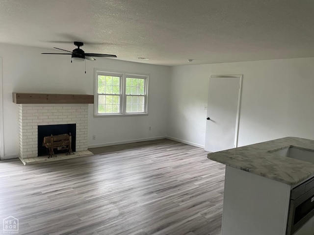 unfurnished living room featuring wood finished floors, baseboards, ceiling fan, a textured ceiling, and a sink