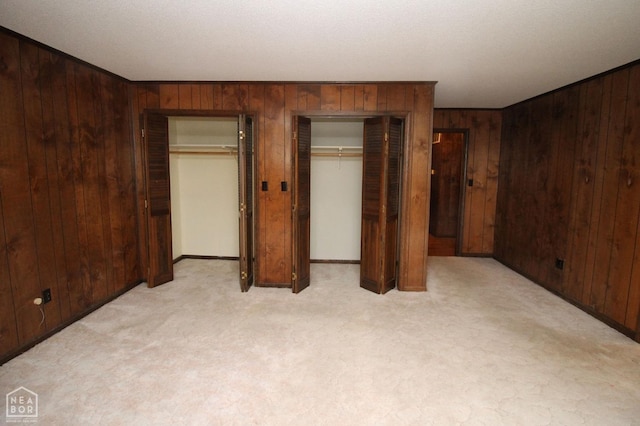 bedroom featuring light carpet, wooden walls, and two closets