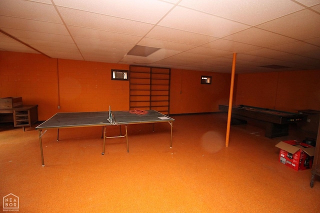 recreation room featuring concrete block wall and a drop ceiling