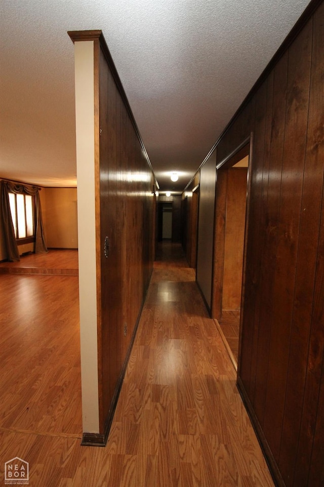 hallway featuring wooden walls, a textured ceiling, crown molding, and wood finished floors