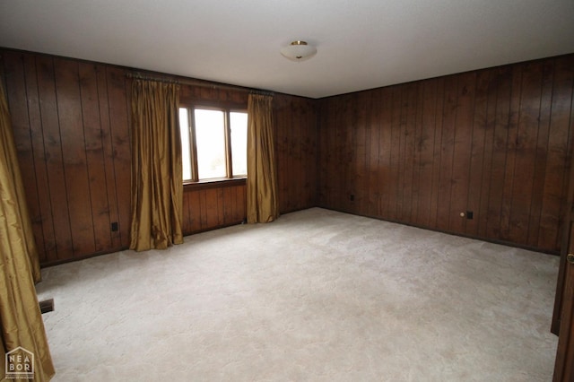 spare room featuring wood walls, visible vents, and light colored carpet