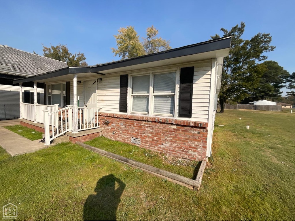view of side of home featuring brick siding, crawl space, covered porch, and a lawn