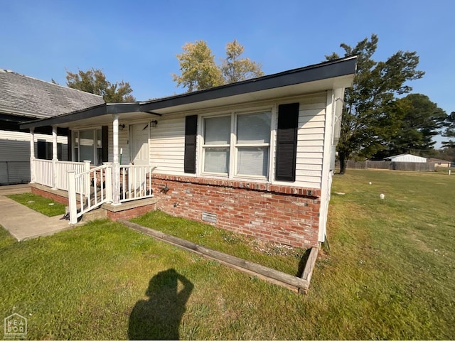 view of side of home featuring brick siding, crawl space, covered porch, and a lawn