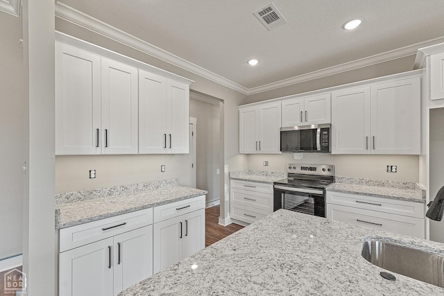 kitchen with white cabinets, visible vents, appliances with stainless steel finishes, ornamental molding, and dark wood-style floors