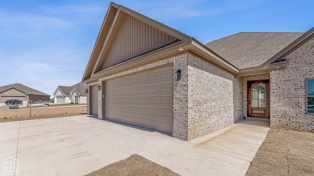 view of property exterior with board and batten siding, roof with shingles, brick siding, and driveway