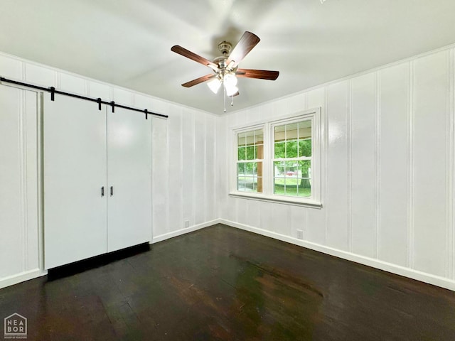 1005 W Lake St, Manila, AR 72442 - unfurnished bedroom with dark wood finished floors, a decorative wall, a barn door, and ceiling fan
