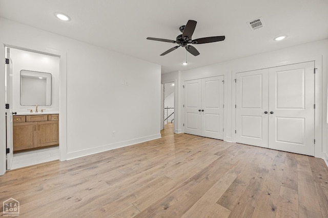 unfurnished bedroom with two closets, visible vents, a sink, light wood finished floors, and baseboards