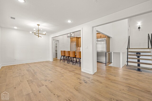 interior space with a notable chandelier, baseboards, stairs, visible vents, and light wood finished floors