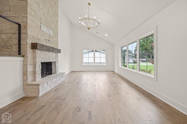 unfurnished living room featuring baseboards, an inviting chandelier, a stone fireplace, hardwood / wood-style flooring, and high vaulted ceiling