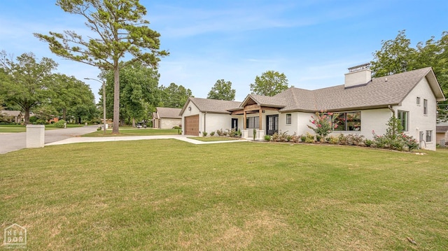 view of front facade with a front yard, a garage, driveway, and a chimney