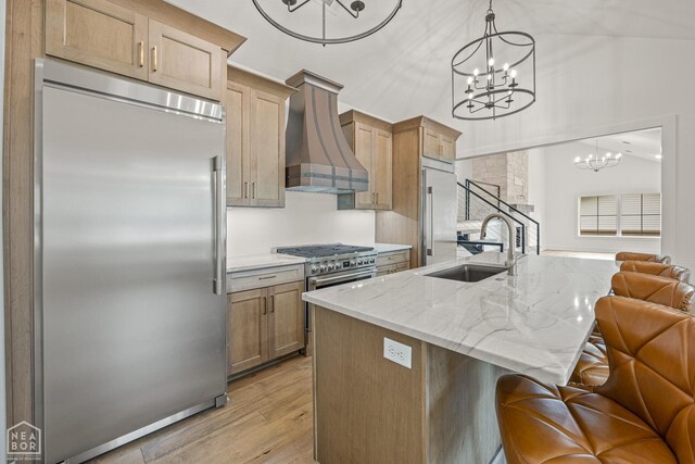 kitchen featuring a sink, high quality appliances, a chandelier, custom range hood, and light wood-style flooring
