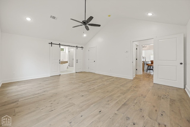 unfurnished living room with light wood-style flooring, a ceiling fan, visible vents, a barn door, and baseboards