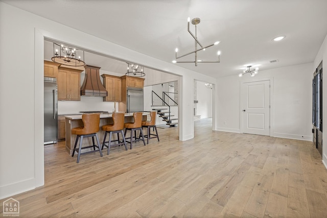 kitchen featuring custom range hood, a notable chandelier, built in fridge, and a kitchen bar