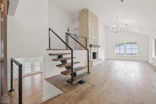 staircase with a chandelier, high vaulted ceiling, a stone fireplace, and hardwood / wood-style flooring