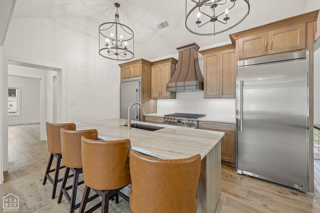kitchen with an inviting chandelier, wall chimney range hood, visible vents, appliances with stainless steel finishes, and a sink