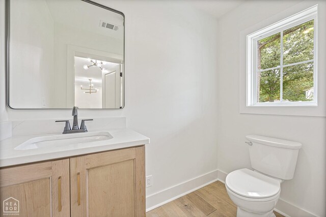 half bathroom with visible vents, baseboards, toilet, vanity, and wood finished floors