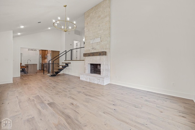 unfurnished living room with baseboards, an inviting chandelier, stairway, high vaulted ceiling, and wood finished floors