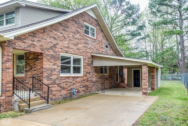 exterior space with a carport, fence, brick siding, a front lawn, and driveway