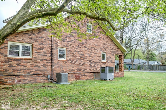 view of home's exterior with central AC, fence, brick siding, and a lawn